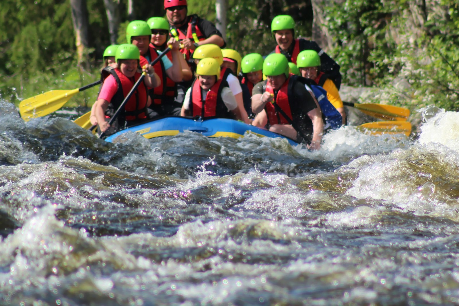 Grupo de chavales con casco y chaleco bajando un río en balsa de rafting
